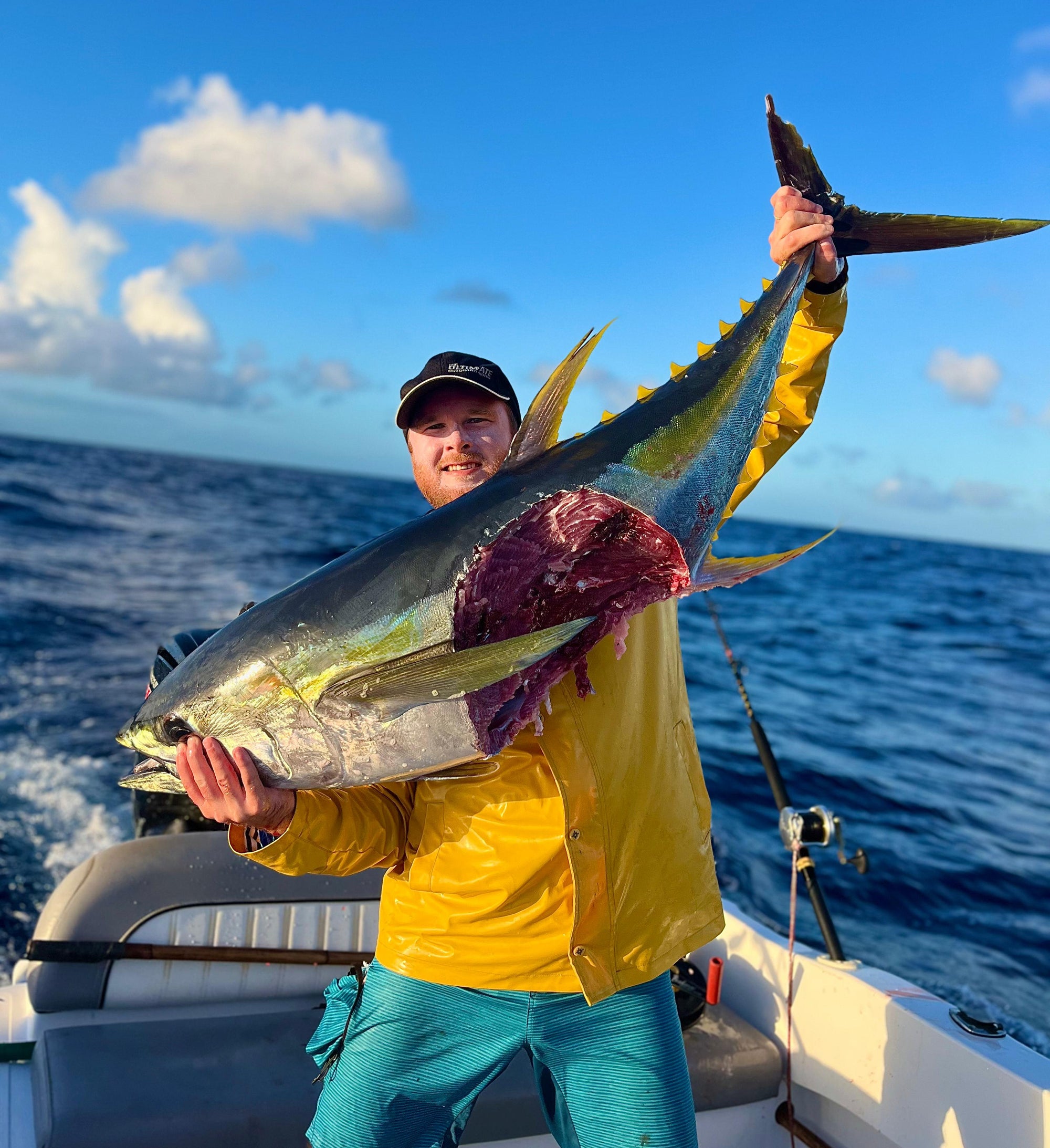 Man holding a large fish on a boat with a blue sky and ocean background